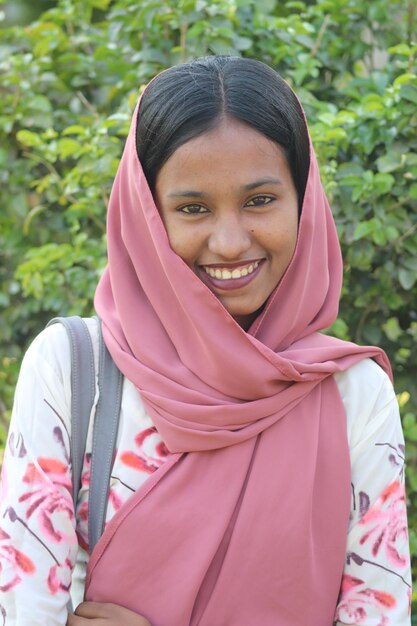 Une femme portant un foulard rose sourit à la caméra.