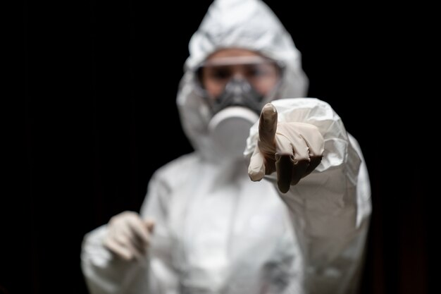 Femme portant des gants avec une combinaison de protection chimique contre les risques biologiques et un masque. Pointant le doigt vers vous