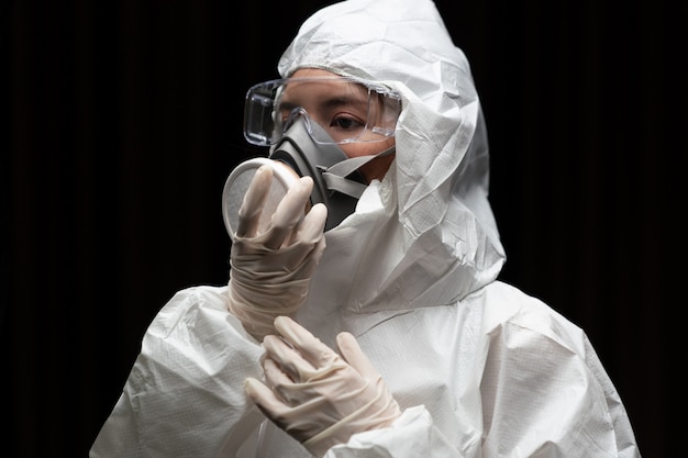 Femme portant des gants avec une combinaison de protection chimique contre les risques biologiques et un masque.