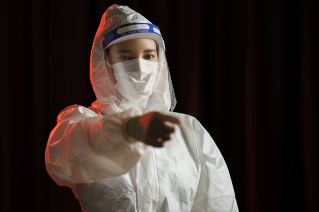 Femme portant des gants, combinaison de protection contre les risques biologiques, écran facial et masque Pointant le doigt vers vous, protection contre les virus.