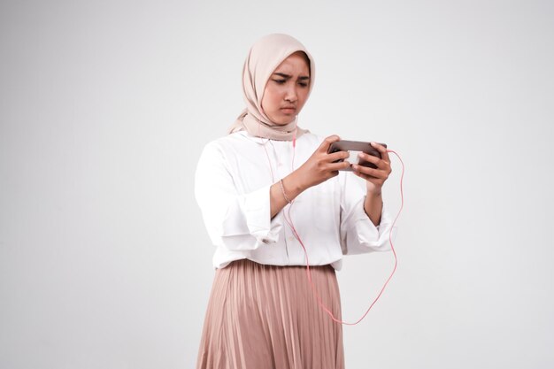 Une femme portant un hijab tient un téléphone et regarde son téléphone.