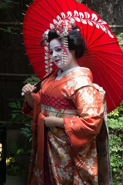 Femme portant un kimono tenant un parapluie rouge alors qu'elle se tient à l'extérieur