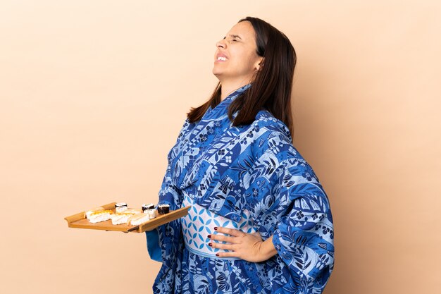 Femme portant un kimono et tenant des sushis sur le mur souffrant de maux de dos pour avoir fait un effort