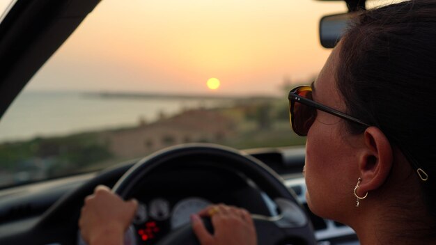 Photo une femme portant des lunettes de soleil conduit une voiture avec le soleil derrière elle