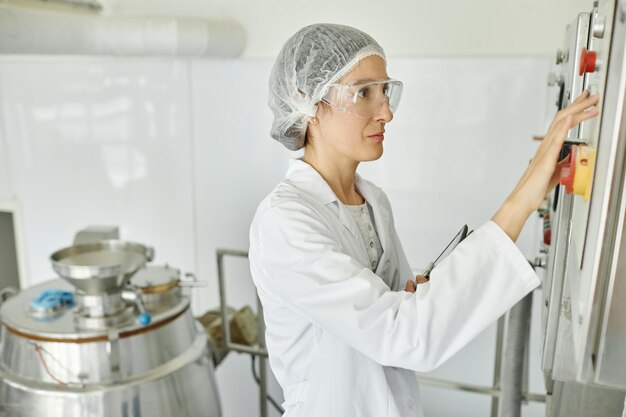 Une femme portant un manteau de laboratoire exploite l'équipement dans un atelier d'usine