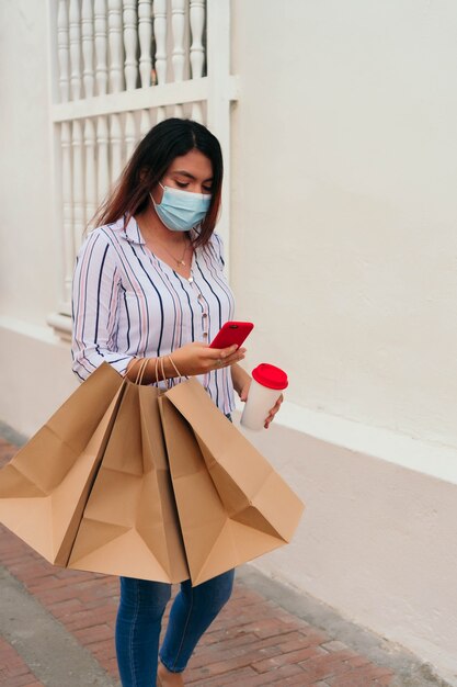 Femme portant un masque à l'aide d'un smartphone tout en se tenant dans la rue de la ville