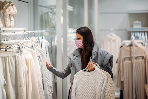 Femme portant un masque facial choisit des vêtements dans un magasin de vêtements