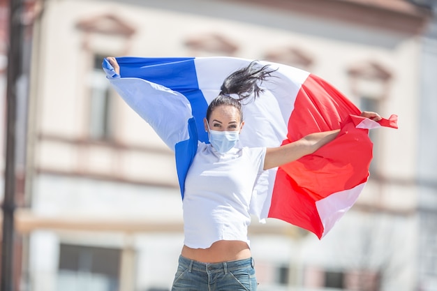 Une femme portant un masque facial tient un drapeau français dans la rue, célébrant une victoire.