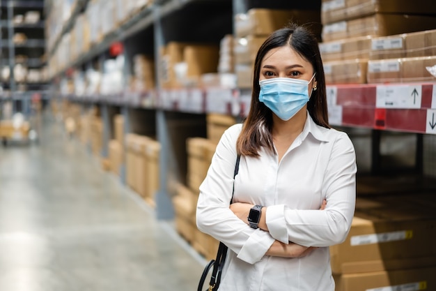 Femme portant un masque médical avec les bras croisés dans le magasin de l'entrepôt pendant la pandémie de coronavirus