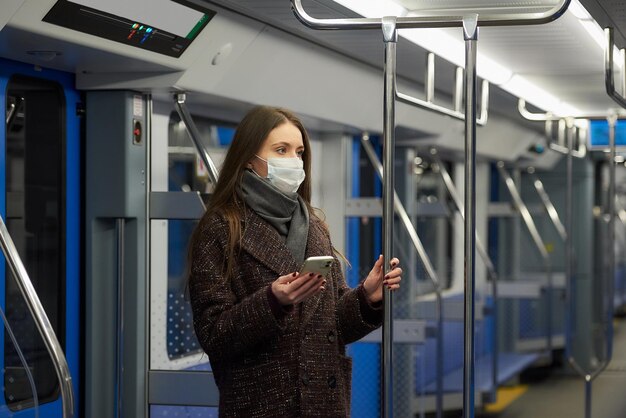 Une femme portant un masque médical pour éviter la propagation du coronavirus est debout et tient un téléphone