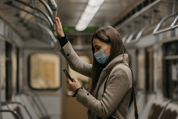 Une femme portant un masque médical pour éviter la propagation du coronavirus utilise un smartphone dans une voiture de métro. Une fille portant un masque chirurgical contre le COVID-19 fait défiler les nouvelles sur son téléphone portable dans un train.