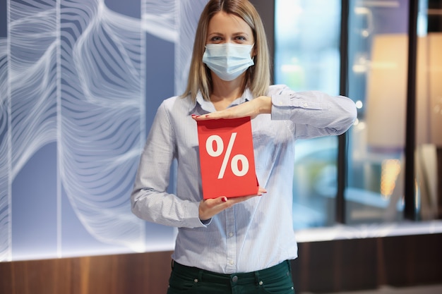 Femme portant un masque médical de protection tenant une pancarte rouge avec des pourcentages de remise en magasin. Concept de promotions et de réductions du vendredi noir