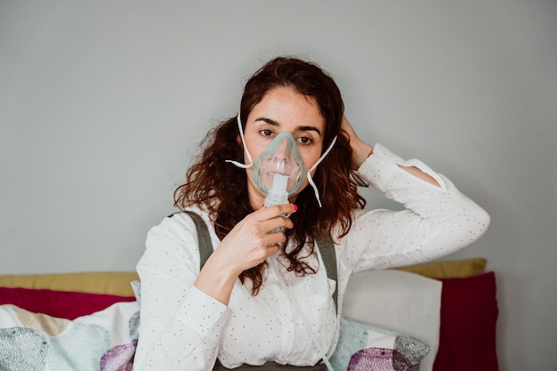 Une femme portant un masque à oxygène alors qu'elle est assise contre le mur à l'hôpital