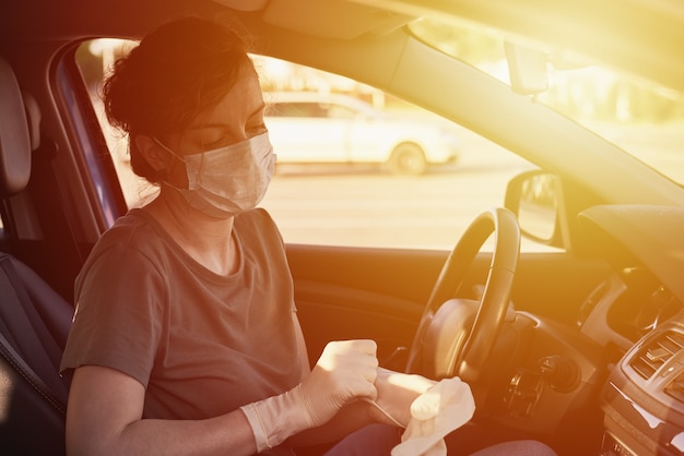 Femme portant un masque de protection et des gants chirurgicaux dans la voiture