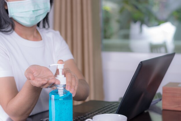 Femme portant un masque de protection. Se nettoyer les mains avec du gel désinfectant. Quarantaine, travail à domicile.