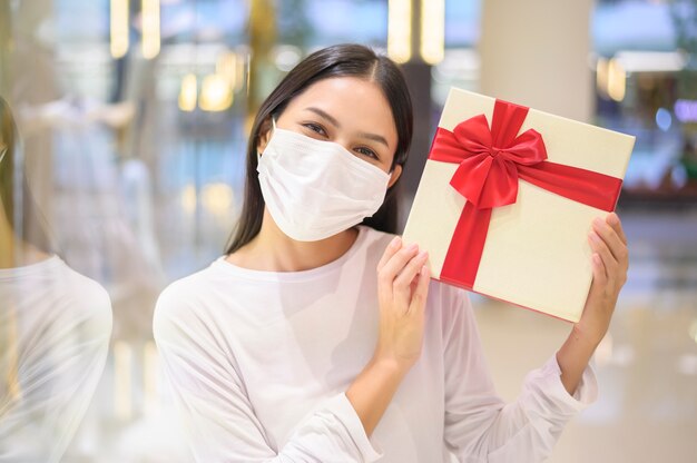 Femme portant un masque de protection tenant une boîte-cadeau dans un centre commercial