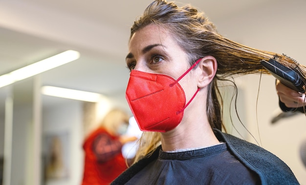 Femme portant un masque rouge se faisant couper les cheveux frais chez un coiffeur pendant la pandémie de covid19
