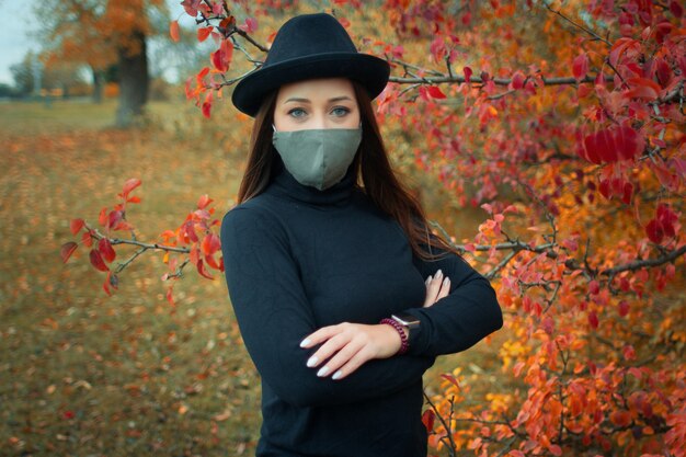 femme portant un masque en tissu et un chapeau posant dans le parc automne