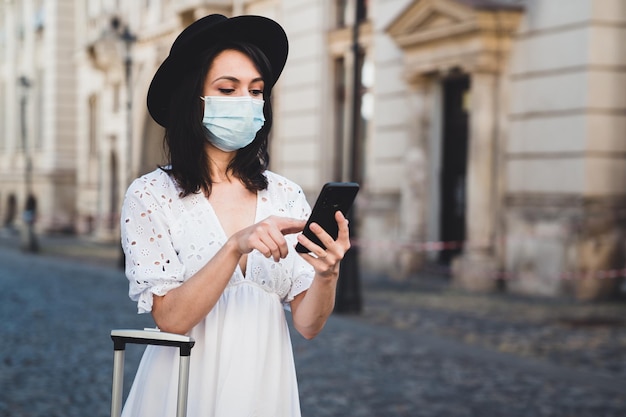 Une femme portant un masque en utilisant un téléphone intelligent debout sur la route