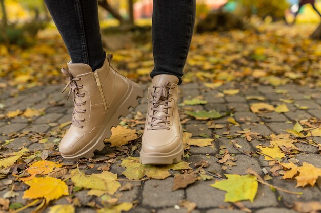 Une femme portant une paire de bottes beiges se tient sur un chemin couvert de feuilles mortes.