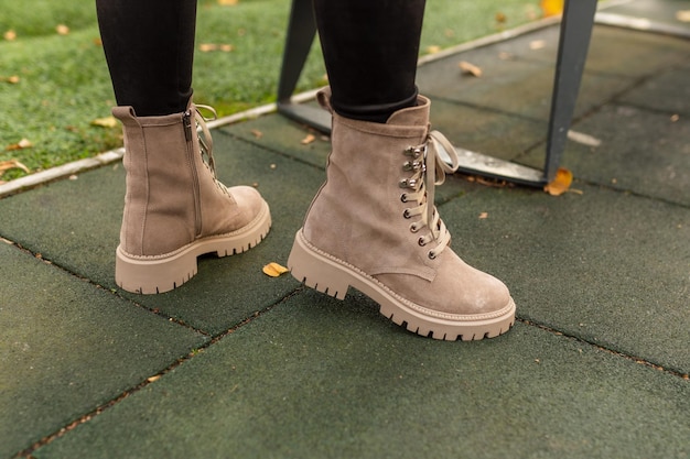 Une femme portant une paire de bottes beiges se tient sur un trottoir.