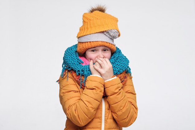 Femme portant plusieurs chapeaux et écharpes d'hiver chauds mordre les ongles