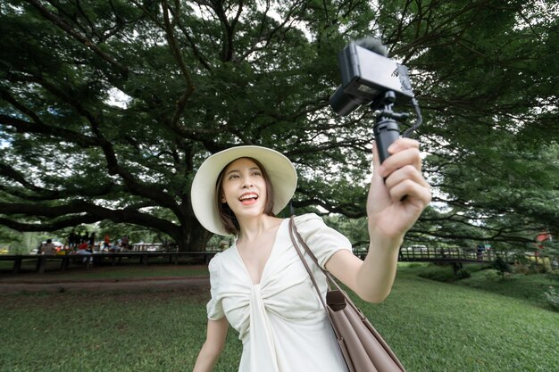 Femme portant une robe blanche prenant selfie sous les arbres Giant Monkey Pod à Kanchanaburi, Thaïlande.