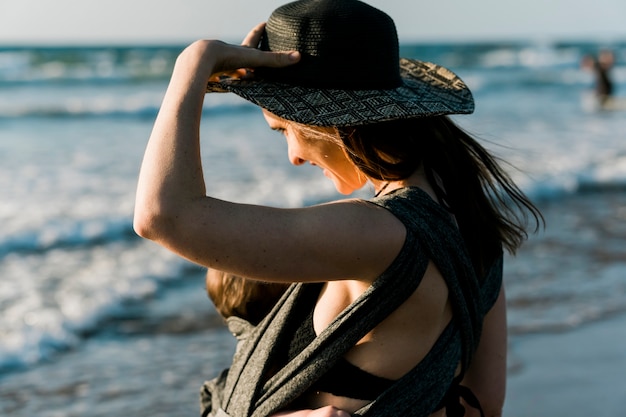 Femme portant son bébé sur la plage en vacances d'été au coucher du soleil