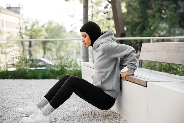 Une femme portant un sweat à capuche gris est assise sur un banc et porte un bonnet noir.