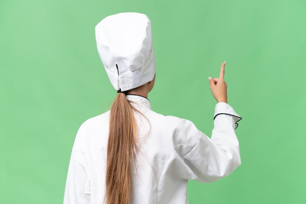 Une femme portant une toque pointe vers un écran vert.