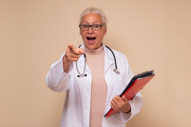 Femme portant un uniforme de médecin tenant des papiers et pointant vers vous avec l'index