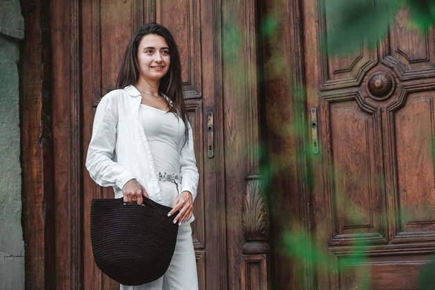 Femme portant des vêtements blancs tenant un sac tricoté sur fond de vieilles portes en bois