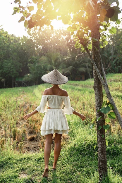 Femme portant des vêtements naturels et un chapeau conique asiatique dans la rizière au coucher du soleil