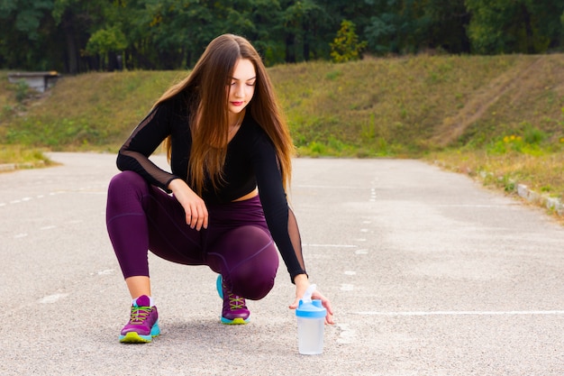 Une femme portant des vêtements de sport prend une pause pour boire de l'eau.