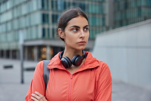 une femme porte un coupe-vent porte un casque stéréo autour du cou revient de m'entraînement de remise en forme pose à l'extérieur en plein air