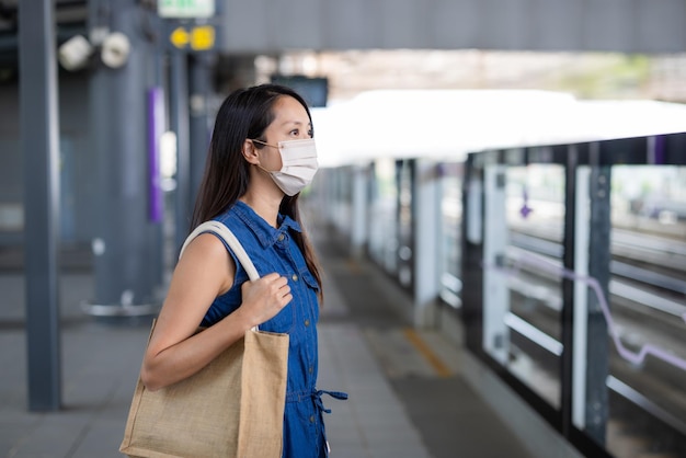 Une femme porte un masque et attend le train.