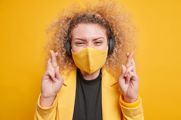 une femme porte un masque protecteur contre le coronavirus souhaite bonne chance garde les doigts croisés écoute de la musique via des écouteurs vêtus de vêtements élégants