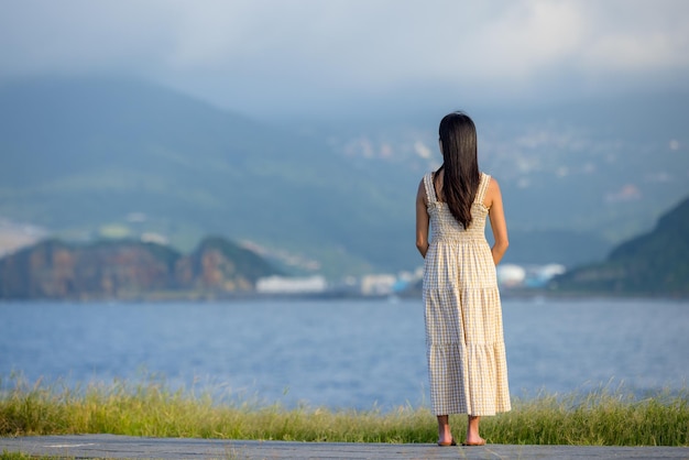 Une femme porte une robe et regarde la mer.