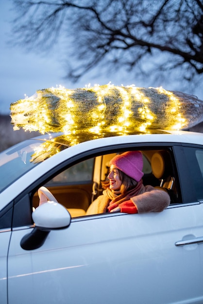 Une femme porte un sapin de Noël en voiture