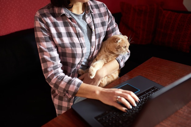 Femme porte un style confortable, travaillant sur un cahier noir et tenant un chat