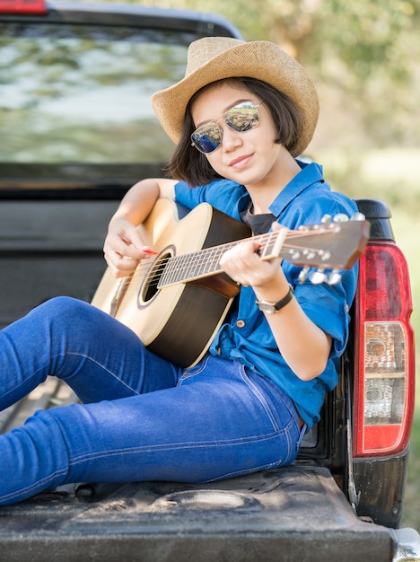 Femme porter un chapeau et jouer de la guitare sur une camionnette