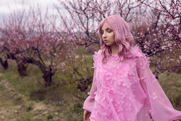 Femme de portrait dans une robe rose avec des fleurs se tient à côté d'un pêcher