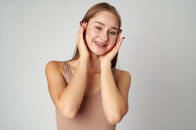 Femme posant avec les mains sur le visage sur un fond gris