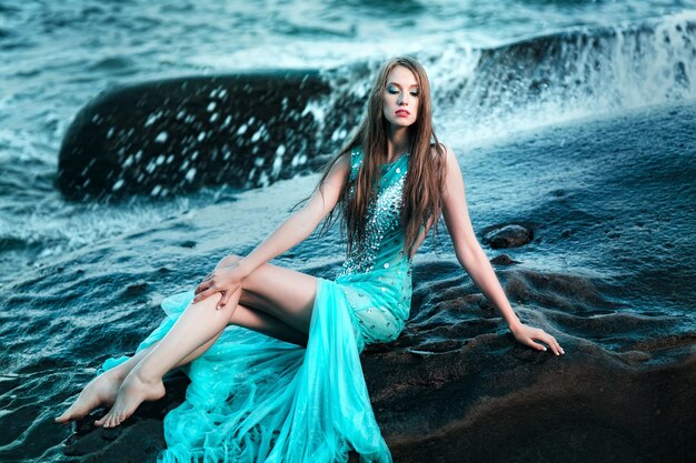 Femme posant sur une plage avec des rochers