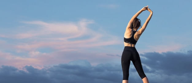 Femme posant en tenue de sport sur fond de ciel. La partie médiane du corps.