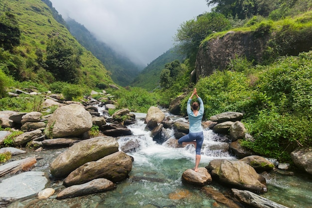 Photo femme en pose d'arbre vrikshasana dans une asana de yoga à la cascade en plein air