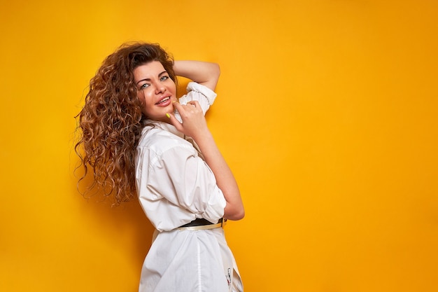 Une femme pose. Une jeune femme heureuse aux cheveux bouclés profite de la vie. Sourit émotionnellement, rit. Elle porte une chemise blanche.