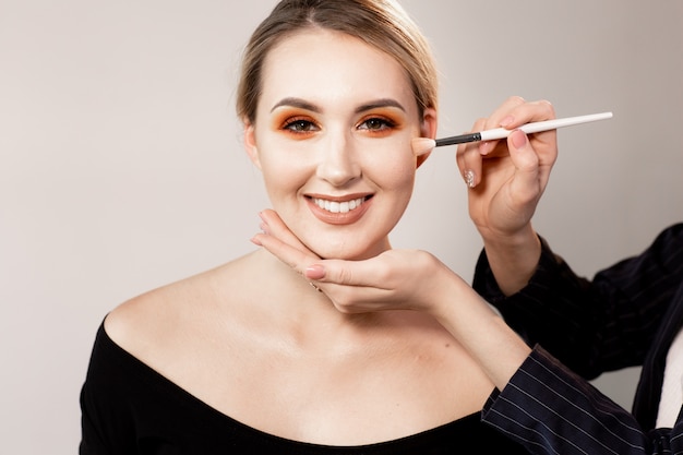 Femme, poser, lumière, studio Les mains du maquilleur corrigent le maquillage avec une brosse spéciale. Maquillage professionnel