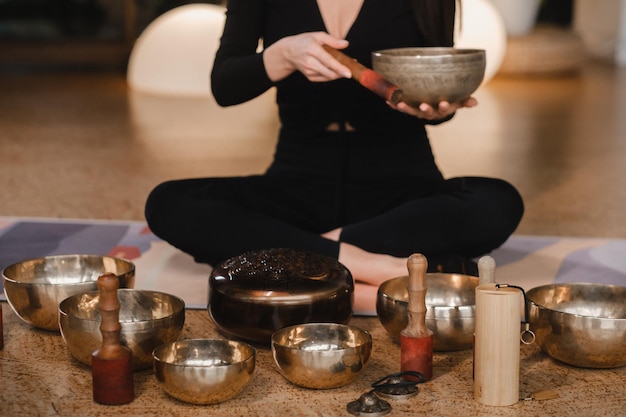 Une femme en position du lotus à l'aide d'un bol chantant à l'intérieur Relaxation et méditation Thérapie par le son médecine alternative Pratiques de guérison bouddhistes