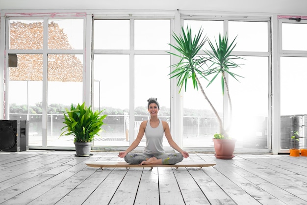 Femme en position du lotus sur planche de SUP à l'intérieur pendant son cours de yoga du matin.